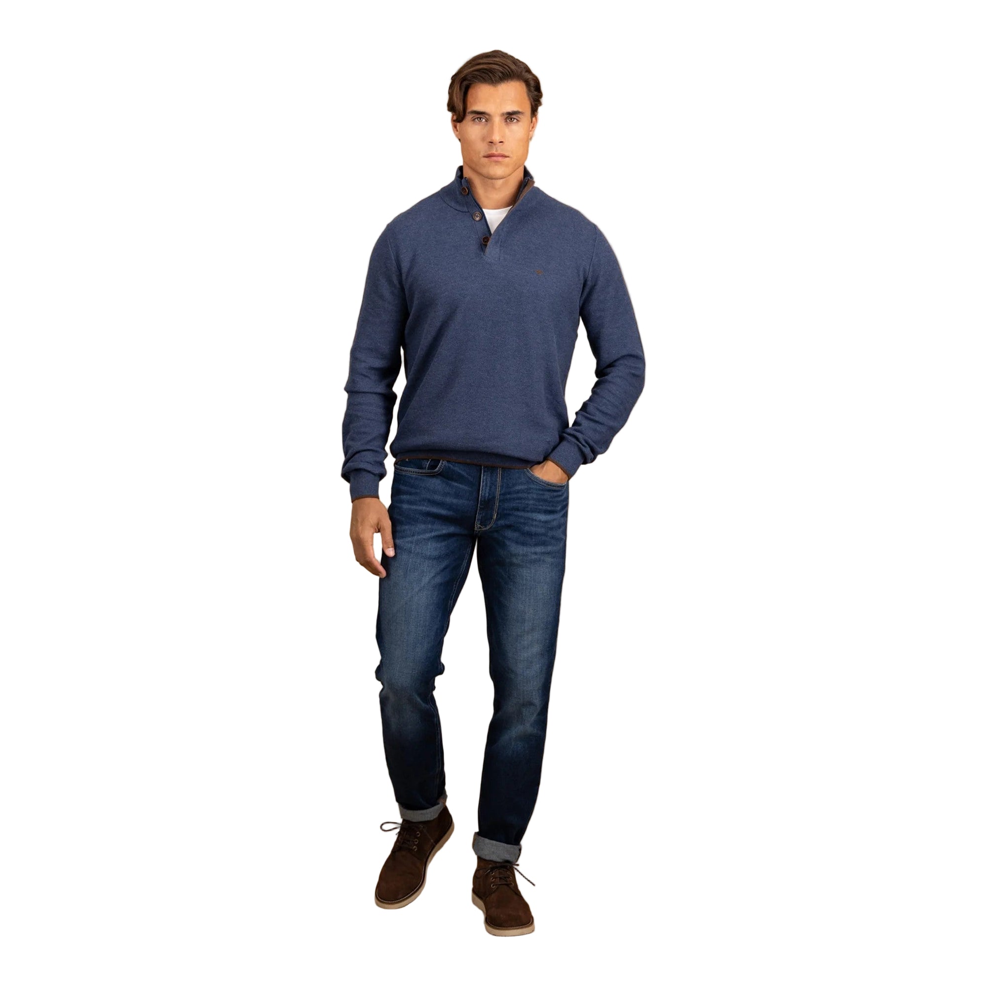 Man wearing a blue sweater and jeans standing against a beige background
