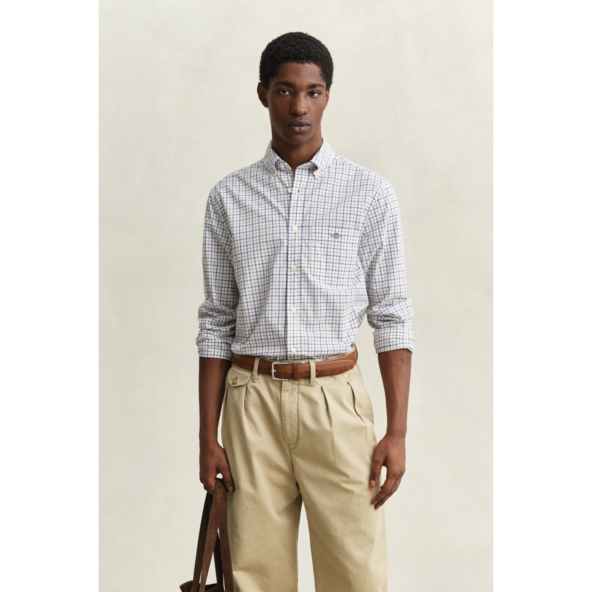 Man wearing a checkered shirt and beige pants against a plain background