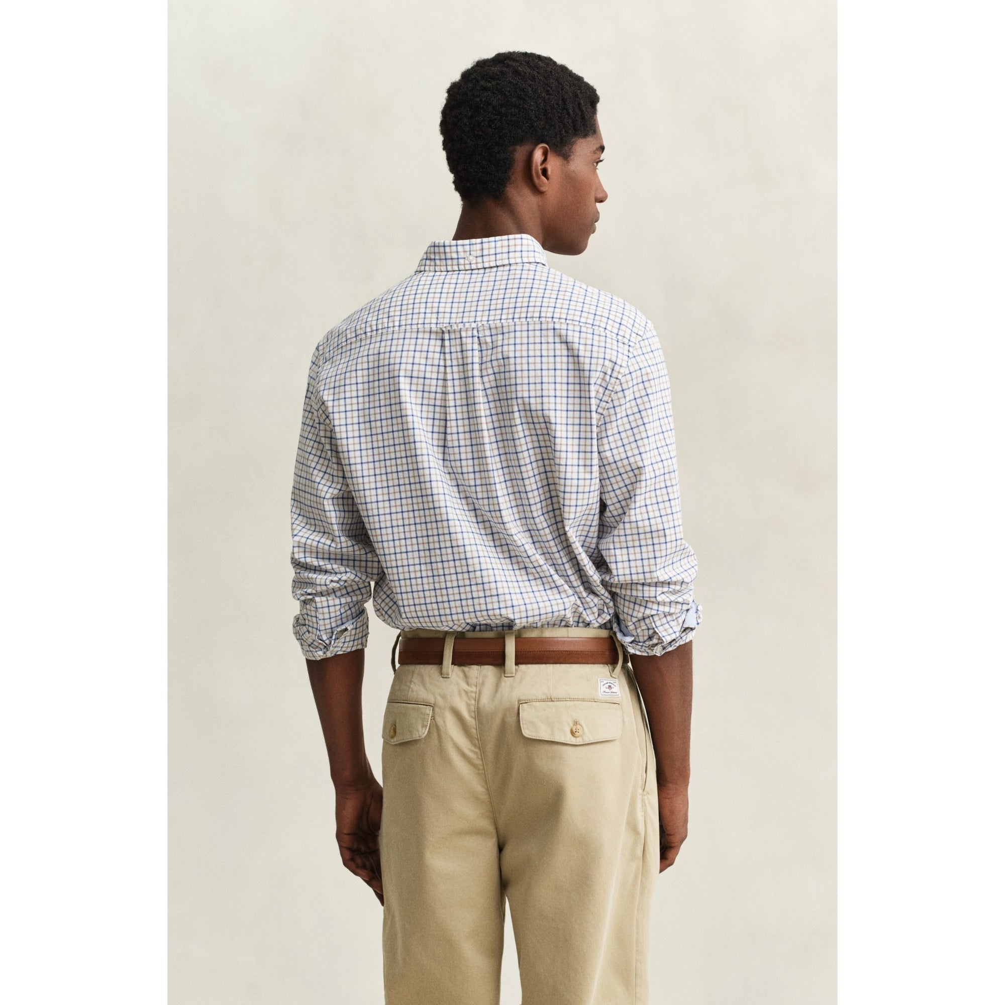 Man wearing a checkered shirt and beige pants against a plain background