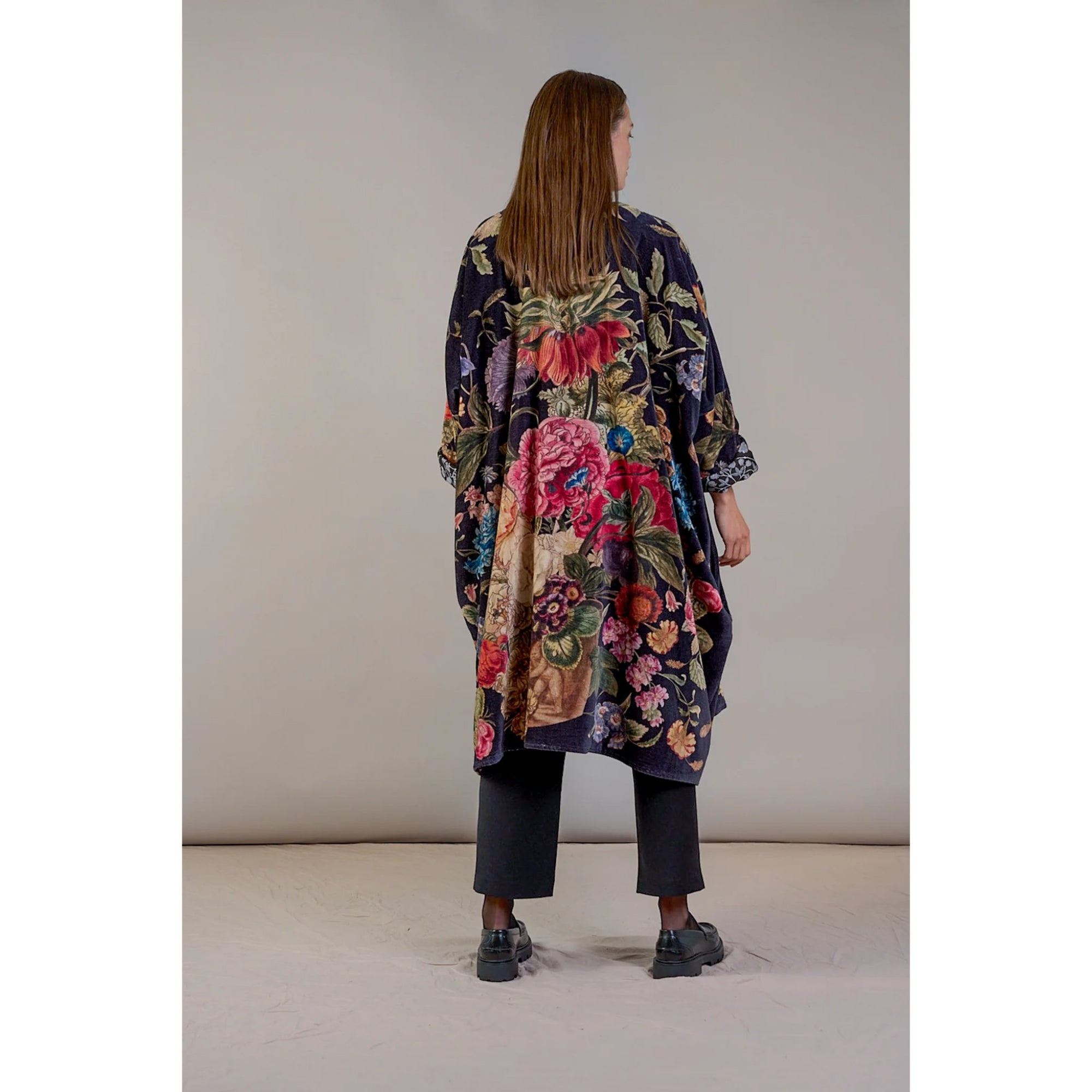 Woman wearing a colorful floral coat against a plain background