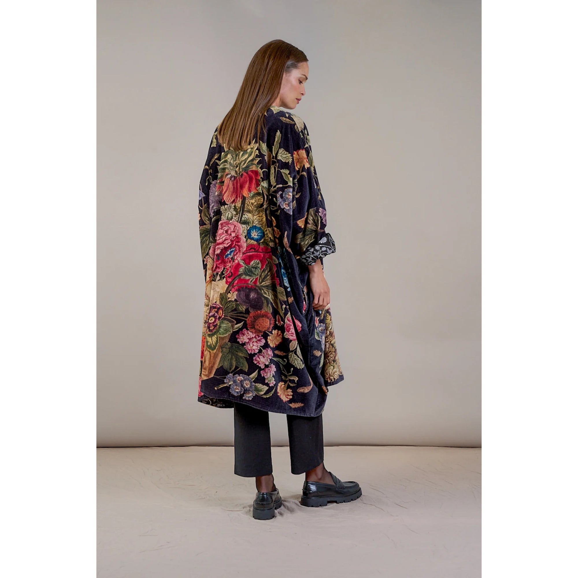 Woman wearing a long, floral-patterned coat against a plain background