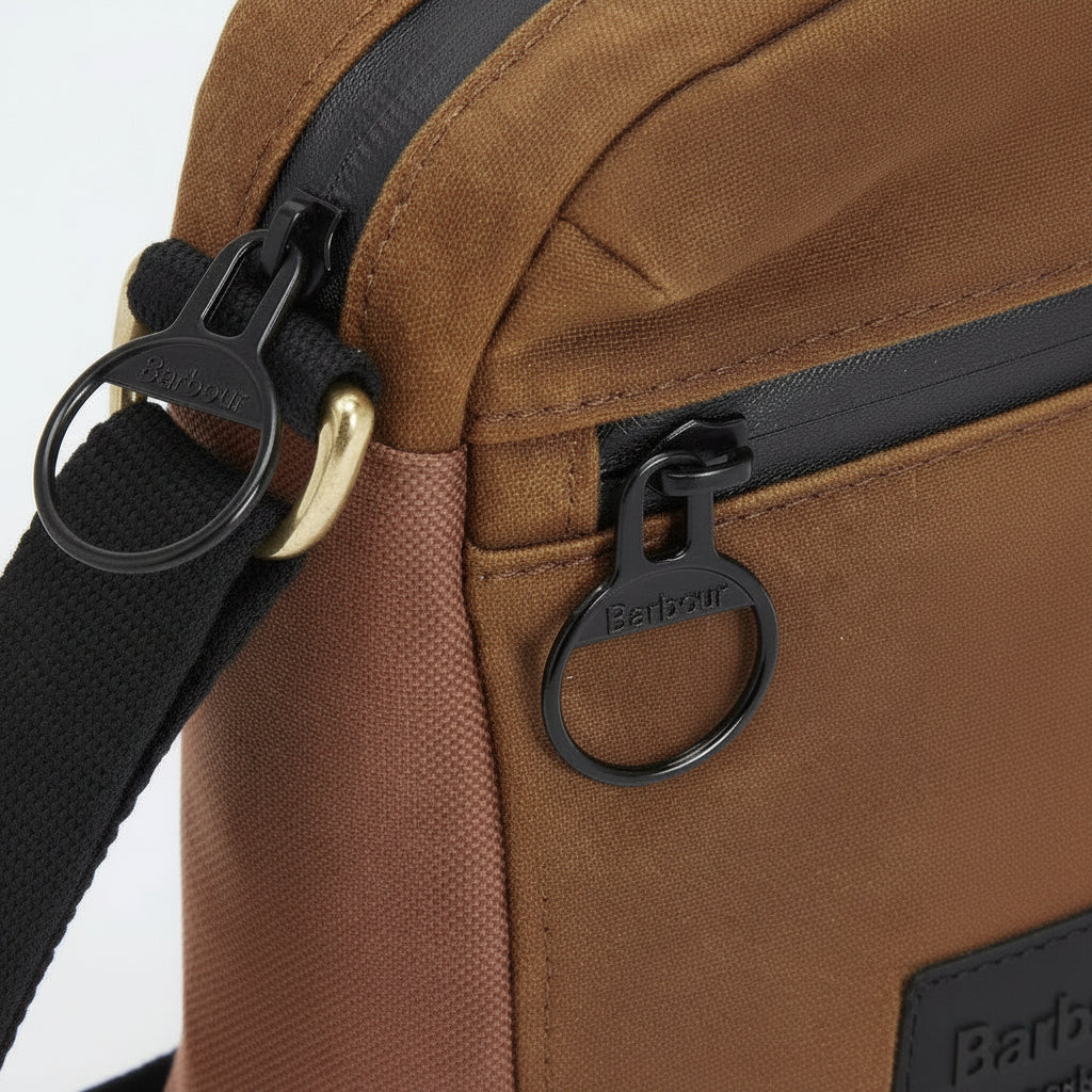 Close-up of a brown canvas crossbody bag with black zippers, black webbing strap, and black oval zipper pulls branded Paracel.