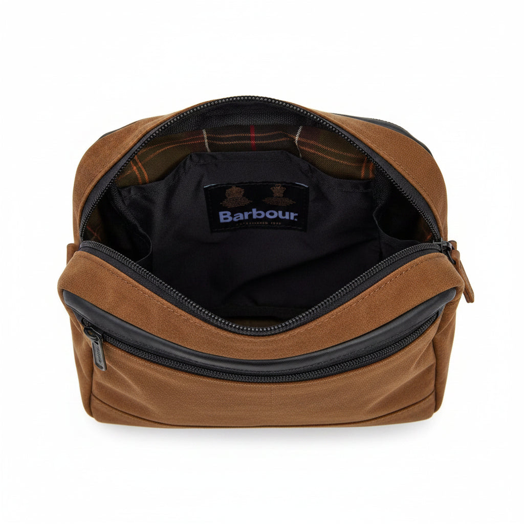 Close-up of the interior of a Barbour bag, showing a black zippered compartment with a black Barbour brand patch and a brown and black plaid lining.
