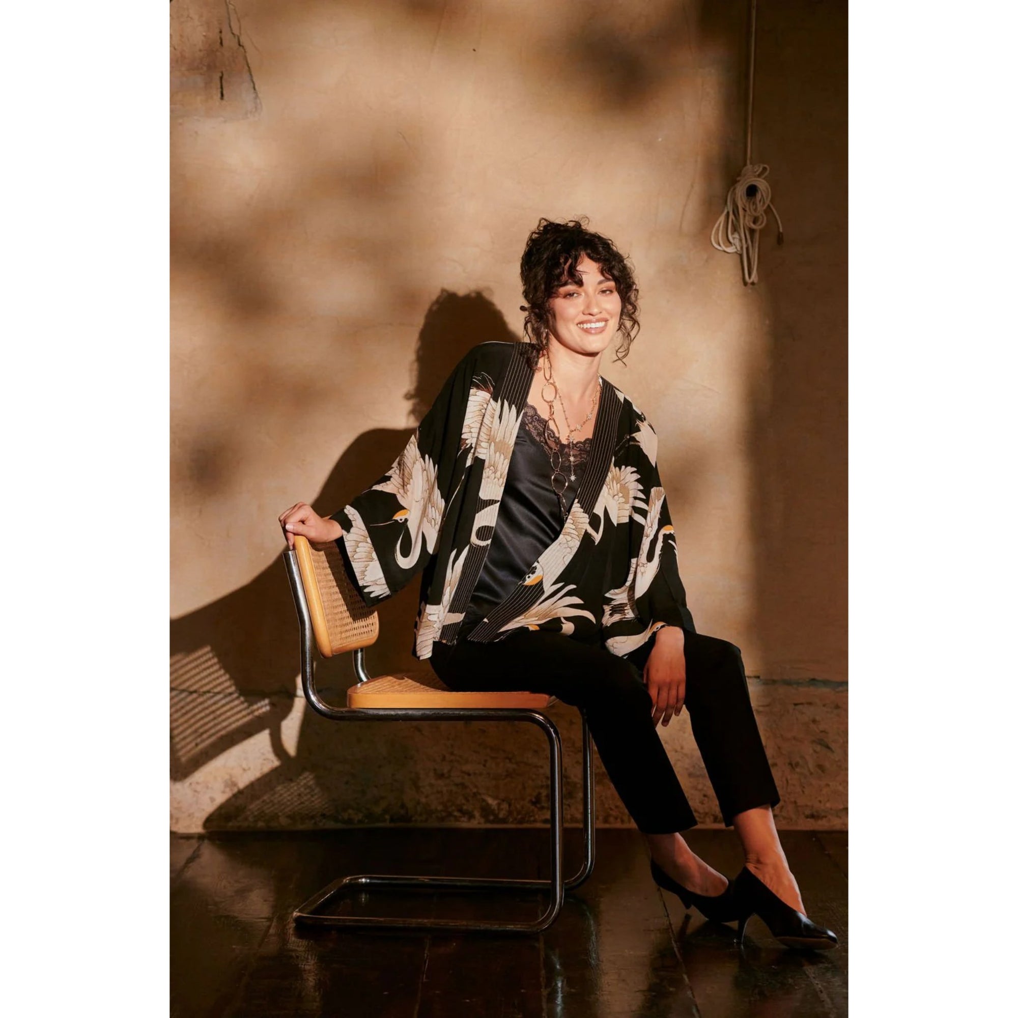 Woman sitting on a chair wearing a patterned jacket in a warm-toned room.