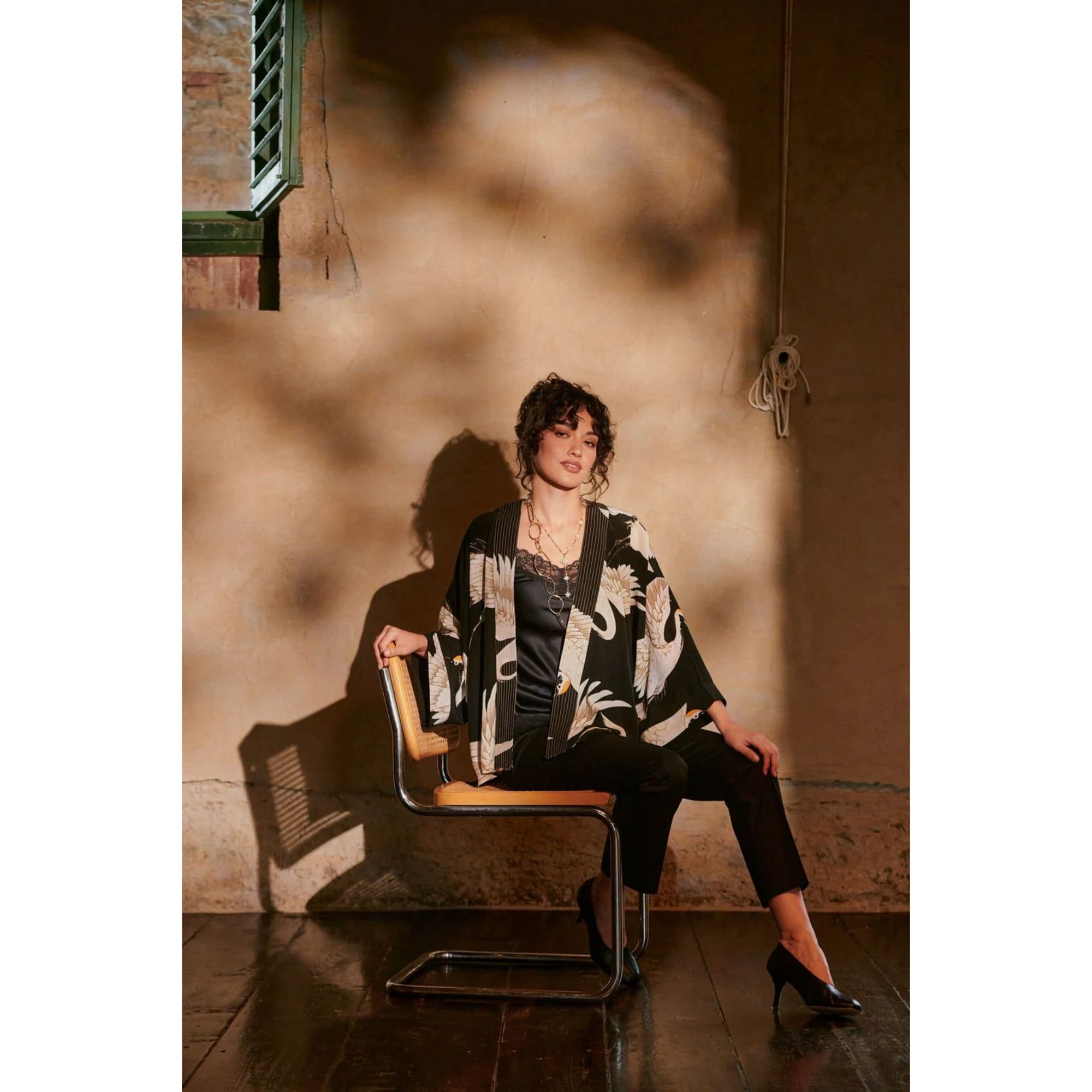 Woman with a kimono sitting on a chair in a room with a textured wall and wooden floor.