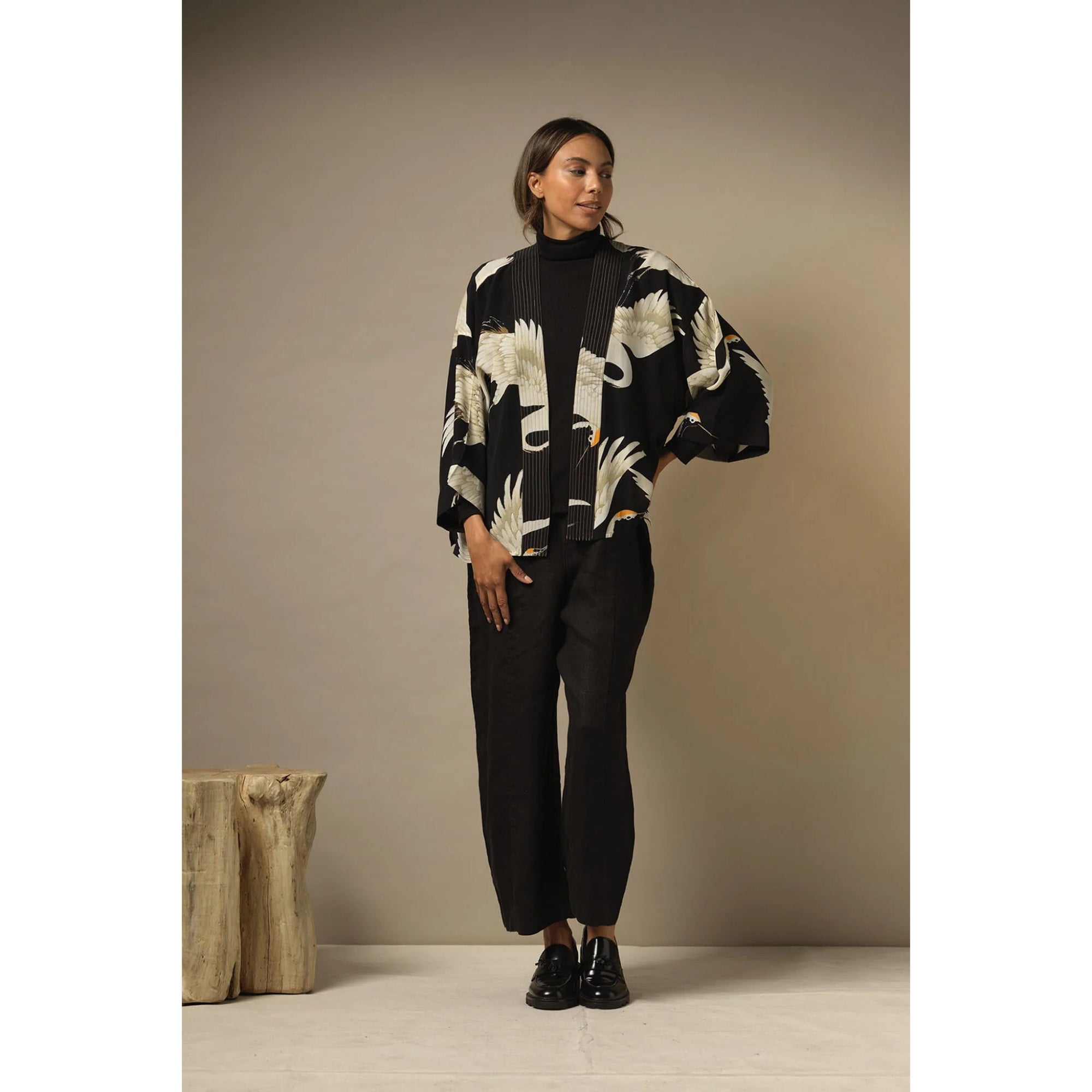 Woman wearing a black and white patterned kimono with black pants against a beige background