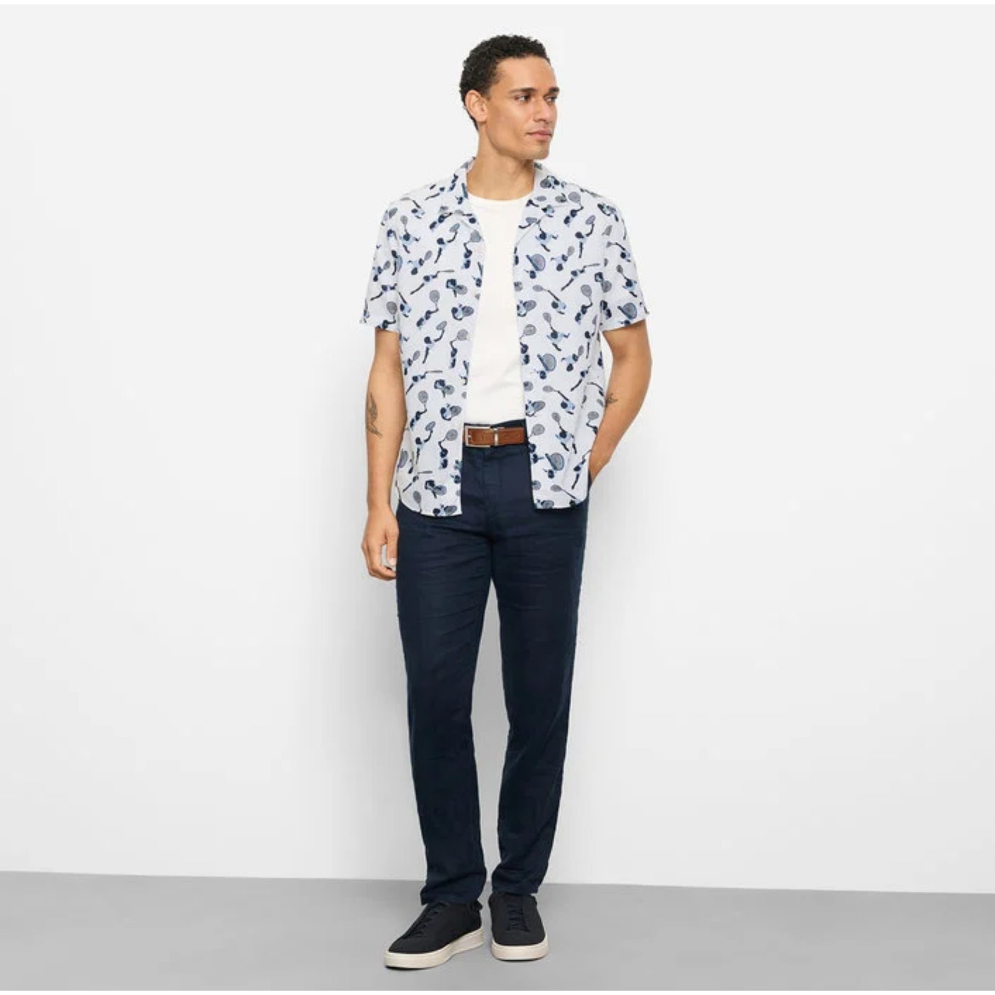 Man wearing a patterned shirt and dark pants against a white background