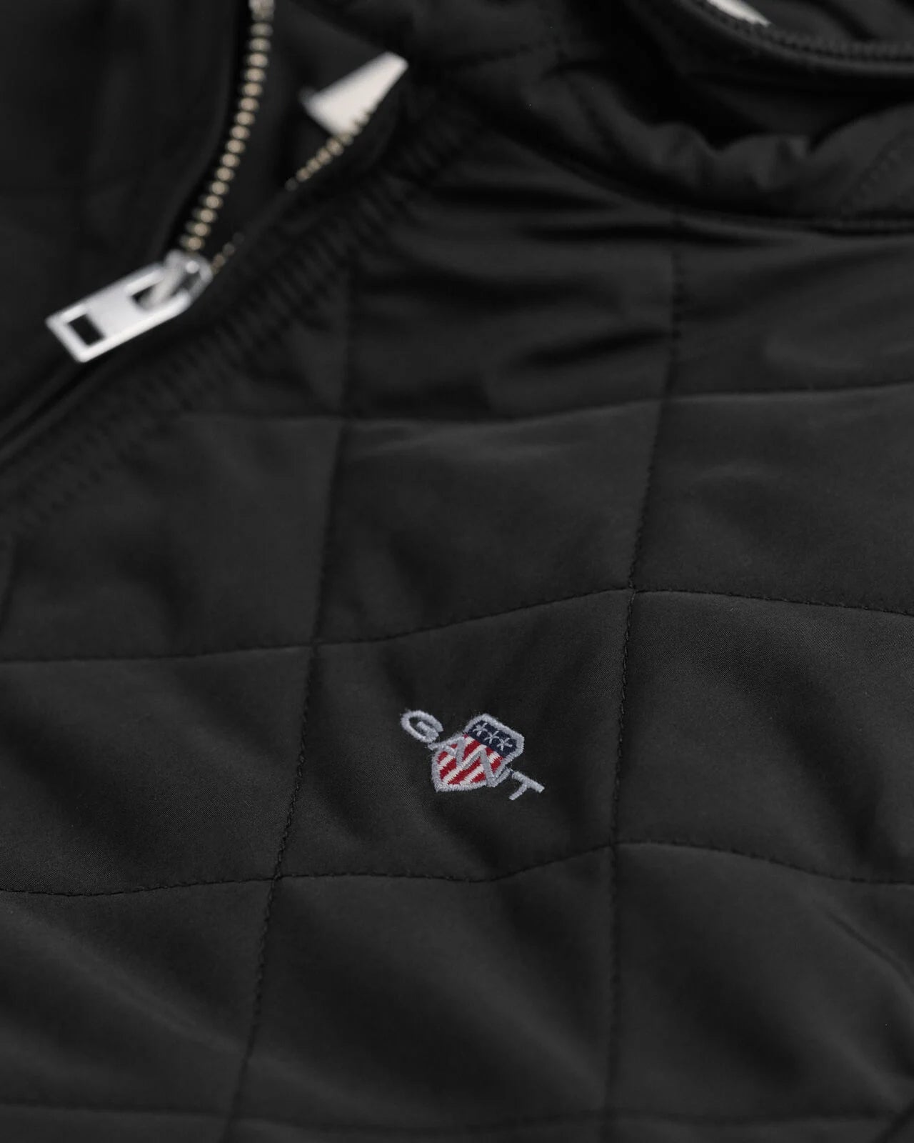 Close-up of a black quilted jacket with a logo on the chest.