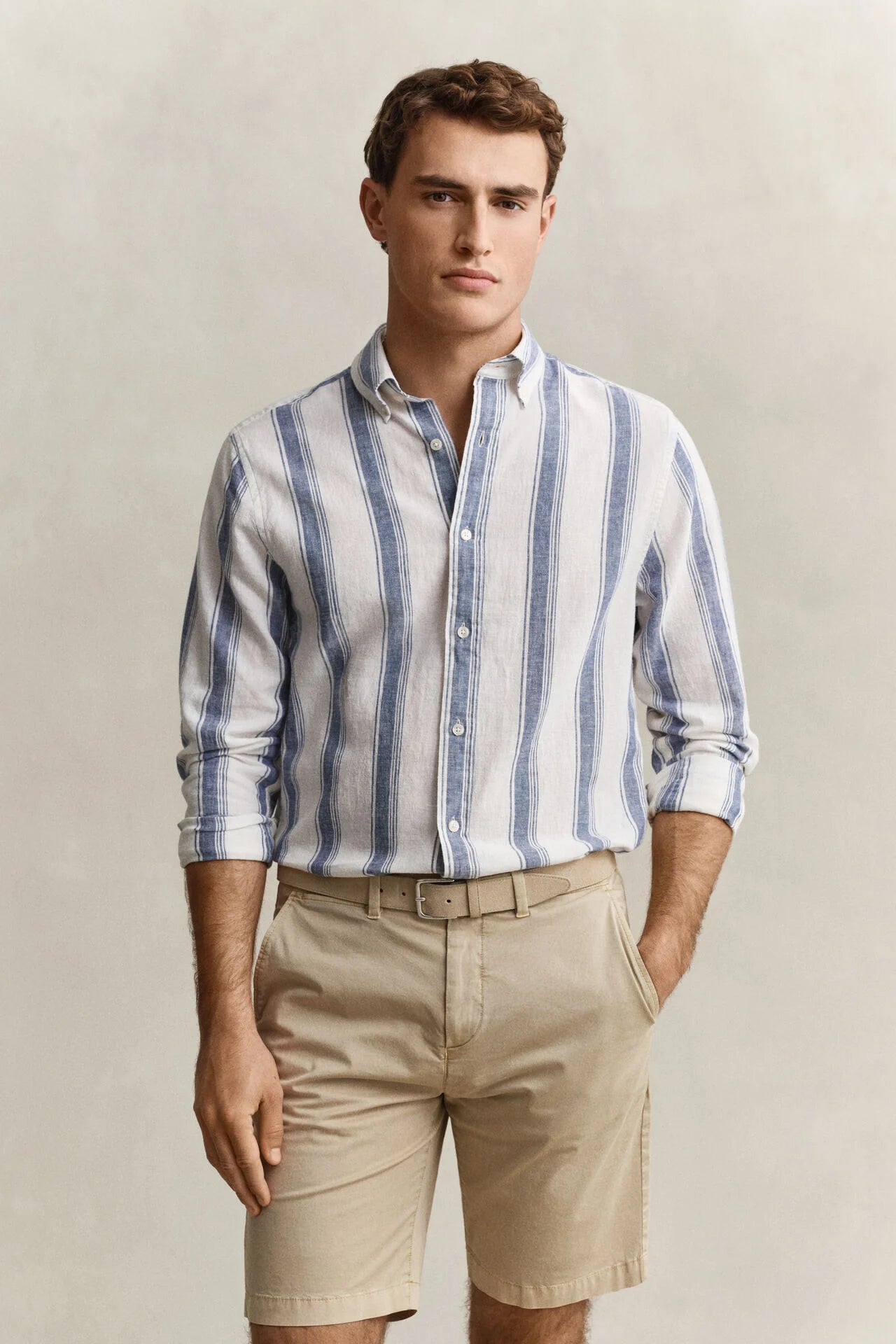 Man wearing a striped shirt and beige shorts against a plain background