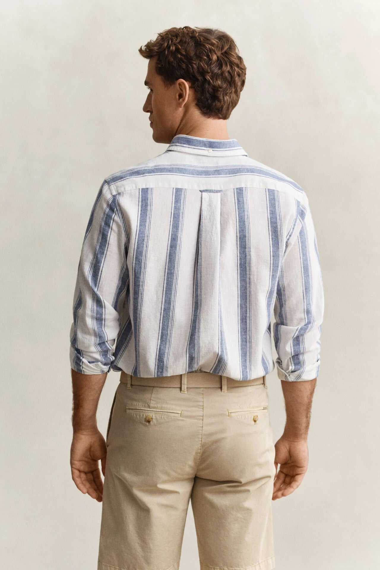 Man wearing a blue and white striped shirt and beige pants against a plain background