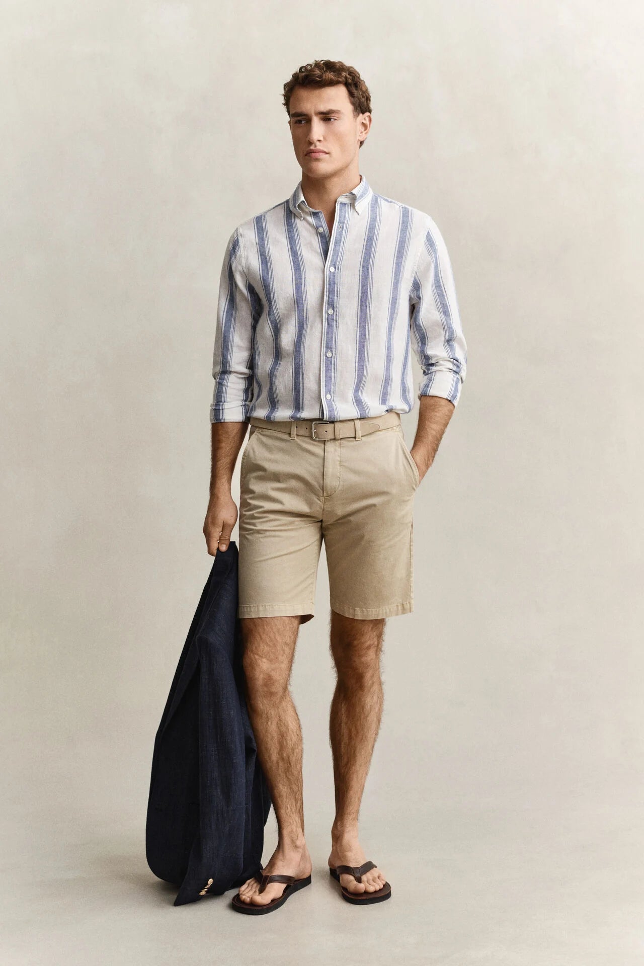 Man wearing a striped shirt and beige shorts against a plain background