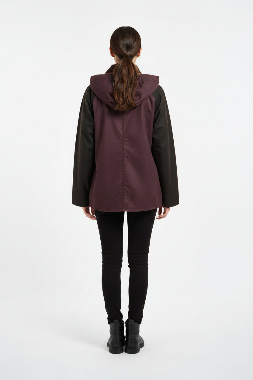 A Barbour hooded jacket with a dark purple body, black sleeves, and a dark brown faux-fur collar and pocket flaps, featuring gold-tone hardware.