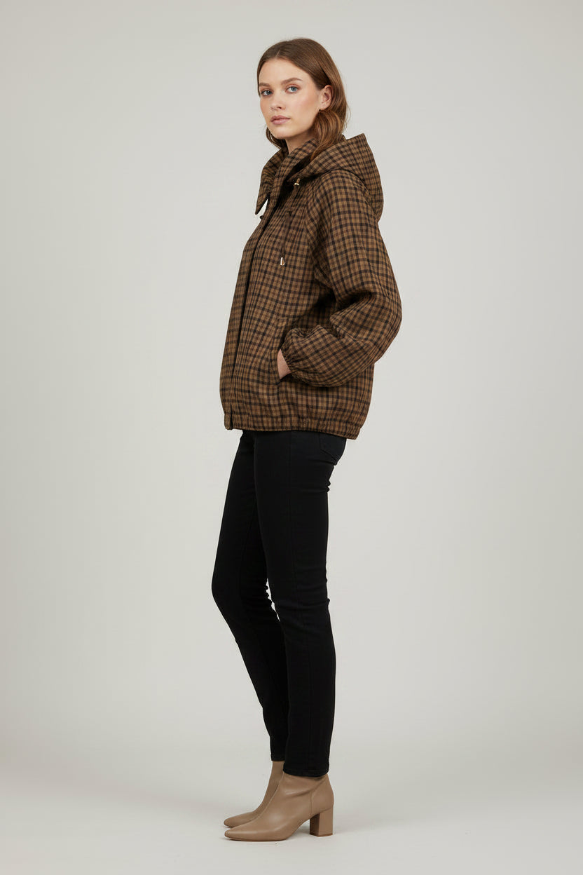 A woman modeling a brown and black plaid hooded jacket with front pockets, paired with black pants and beige ankle boots, against a light gray studio background.