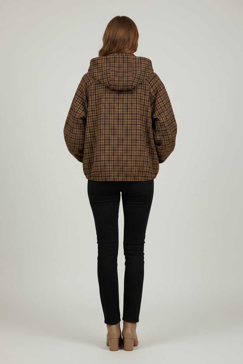 A woman modeling a brown and black plaid hooded jacket with front pockets, paired with black pants and beige ankle boots, against a light gray studio background.