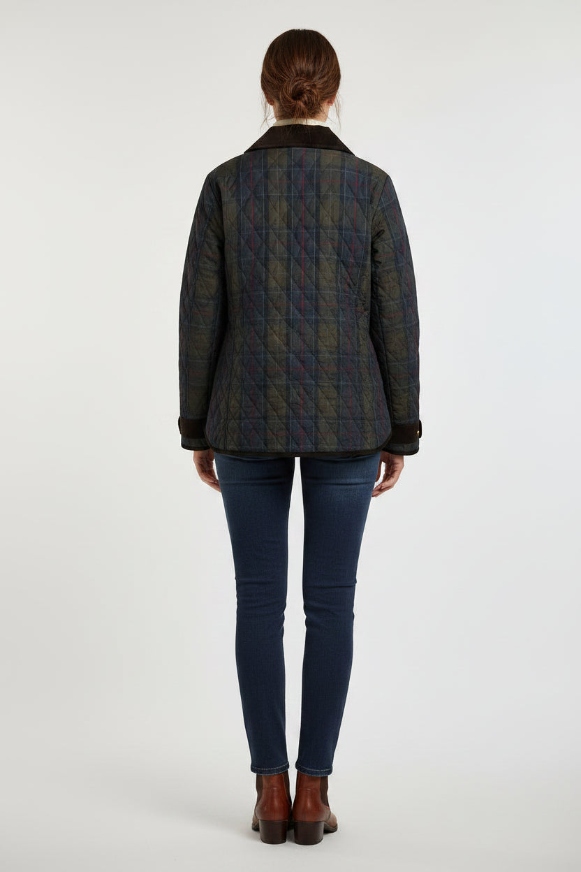 A woman modeling a dark navy quilted jacket with brown faux-fur trim, worn over a cream turtleneck and dark blue skinny jeans, against a light gray studio background.