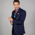 A man wearing a navy blue slim fit 2-piece jacket and waistcoat by Claudio Lugli, with a vibrant patterned tie and a matching handkerchief in his pocket.